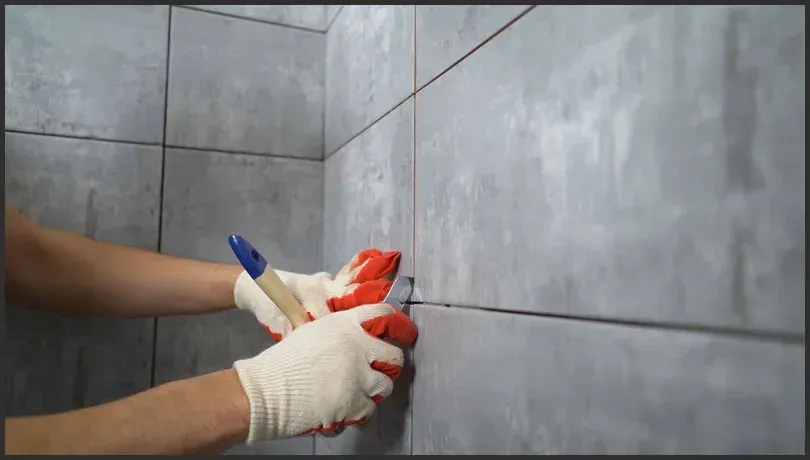 Close-up of a professional cleaning grout between grey tiles using a brush, ensuring fresh and well-maintained bathroom walls.