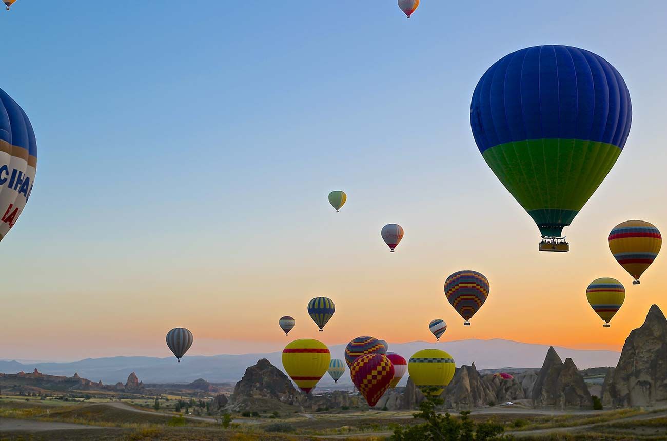 Hot air balloons of various colors floating over a rocky landscape at sunrise.