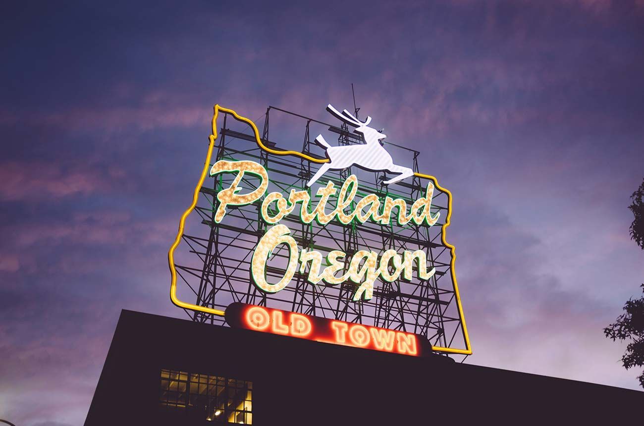 Portland, Oregon sign with white stag silhouette on a map outline, lit up against a dusk sky.