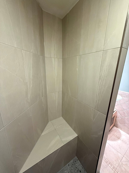 Tiled shower corner with a built-in bench and beige walls, viewed from the doorway