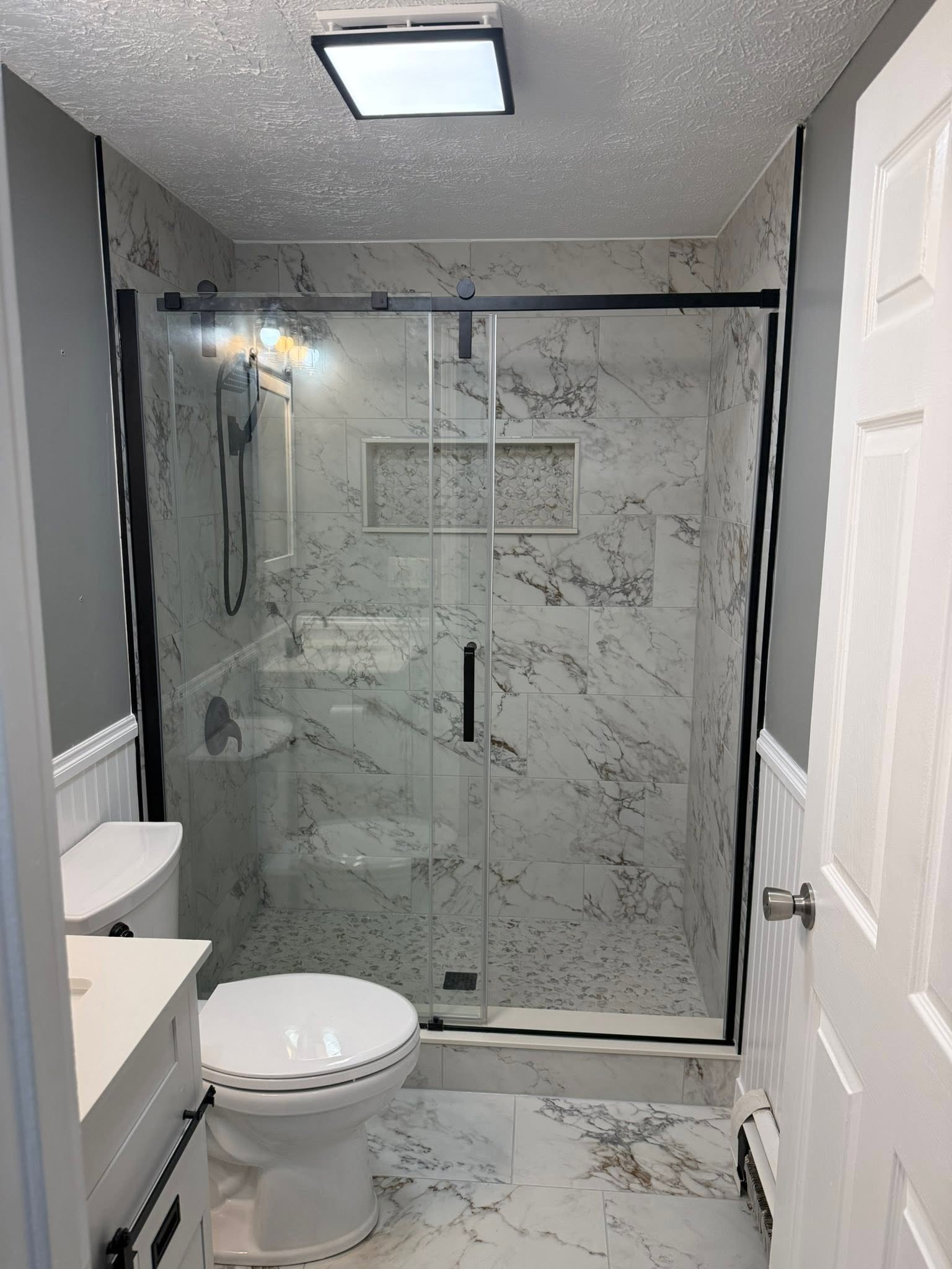 Small bathroom with marble shower, toilet, sink, and gray walls