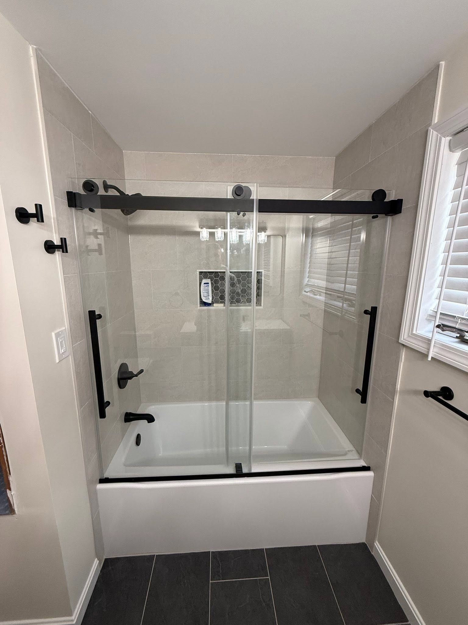 Modern bathroom with a glass shower enclosure, white tub, and dark tile floor
