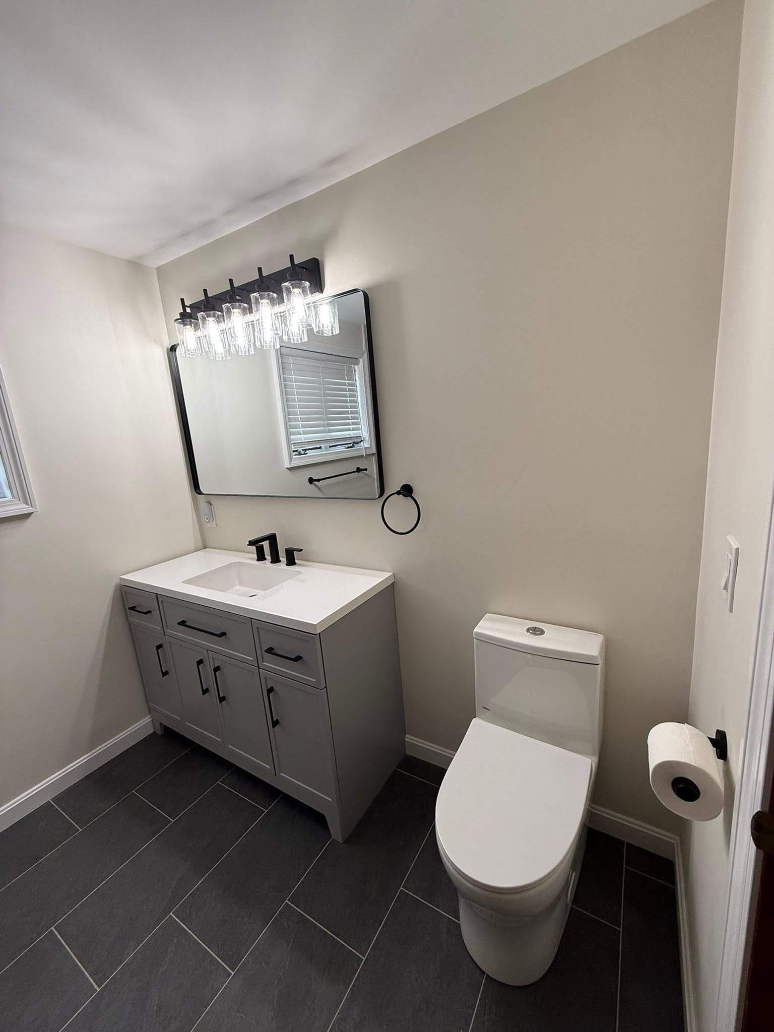 Modern bathroom with gray vanity, mirror, white toilet, and dark tiled floor