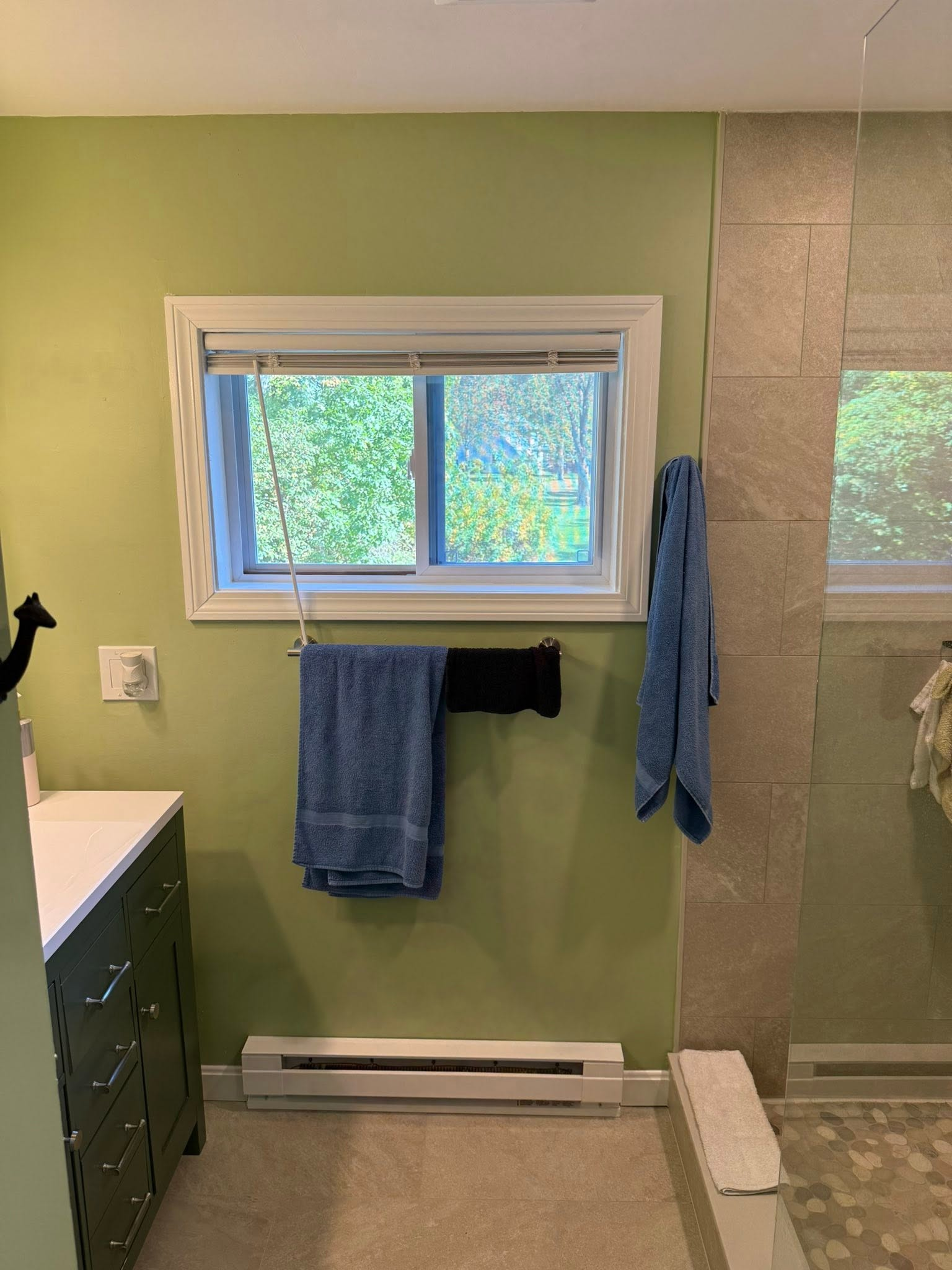 Bathroom with green walls, window, towels on hooks, sink cabinet, and shower/tiled wall on the right.
