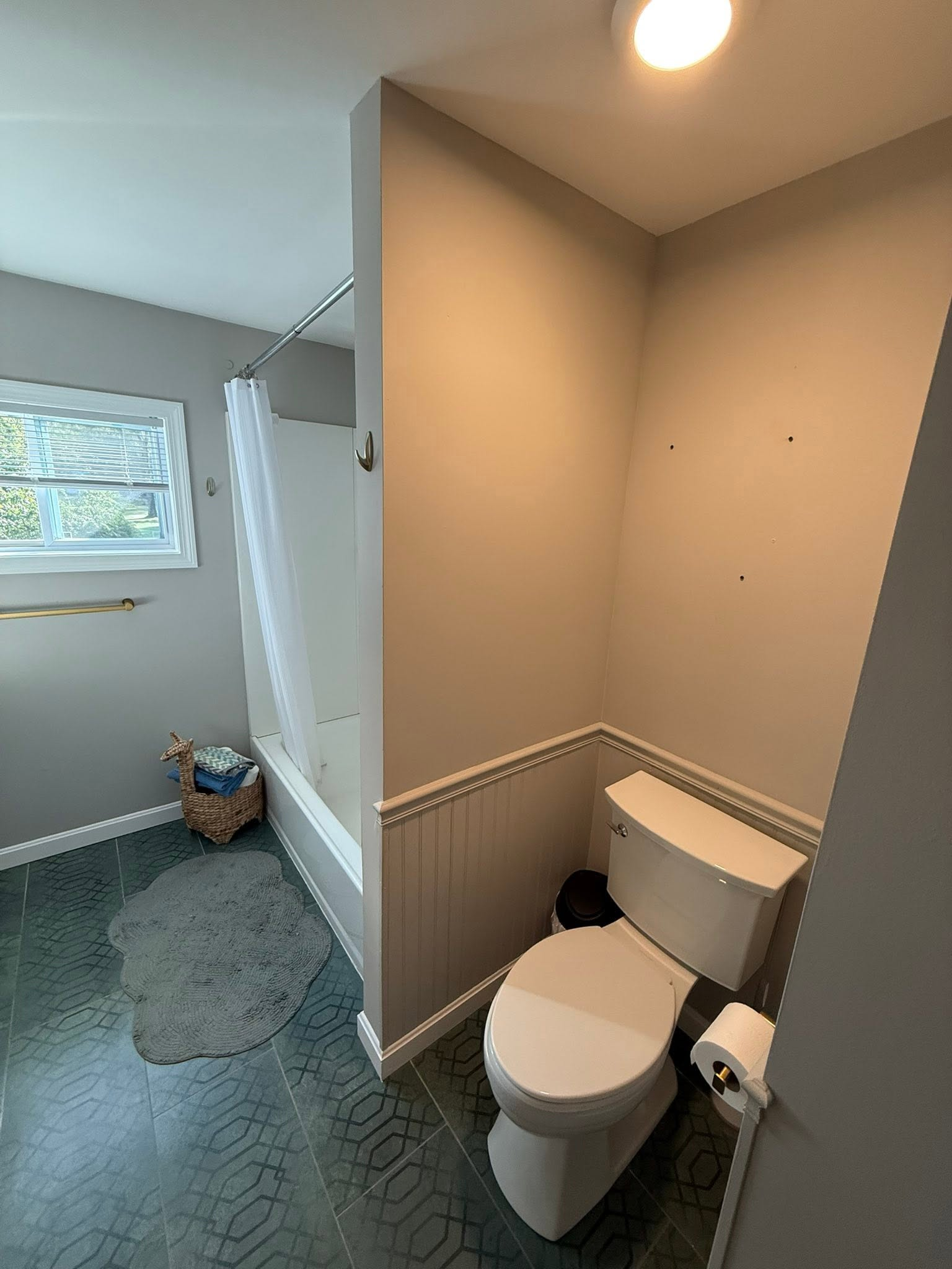 Small bathroom with a toilet, shower curtain, window, and gray rug.