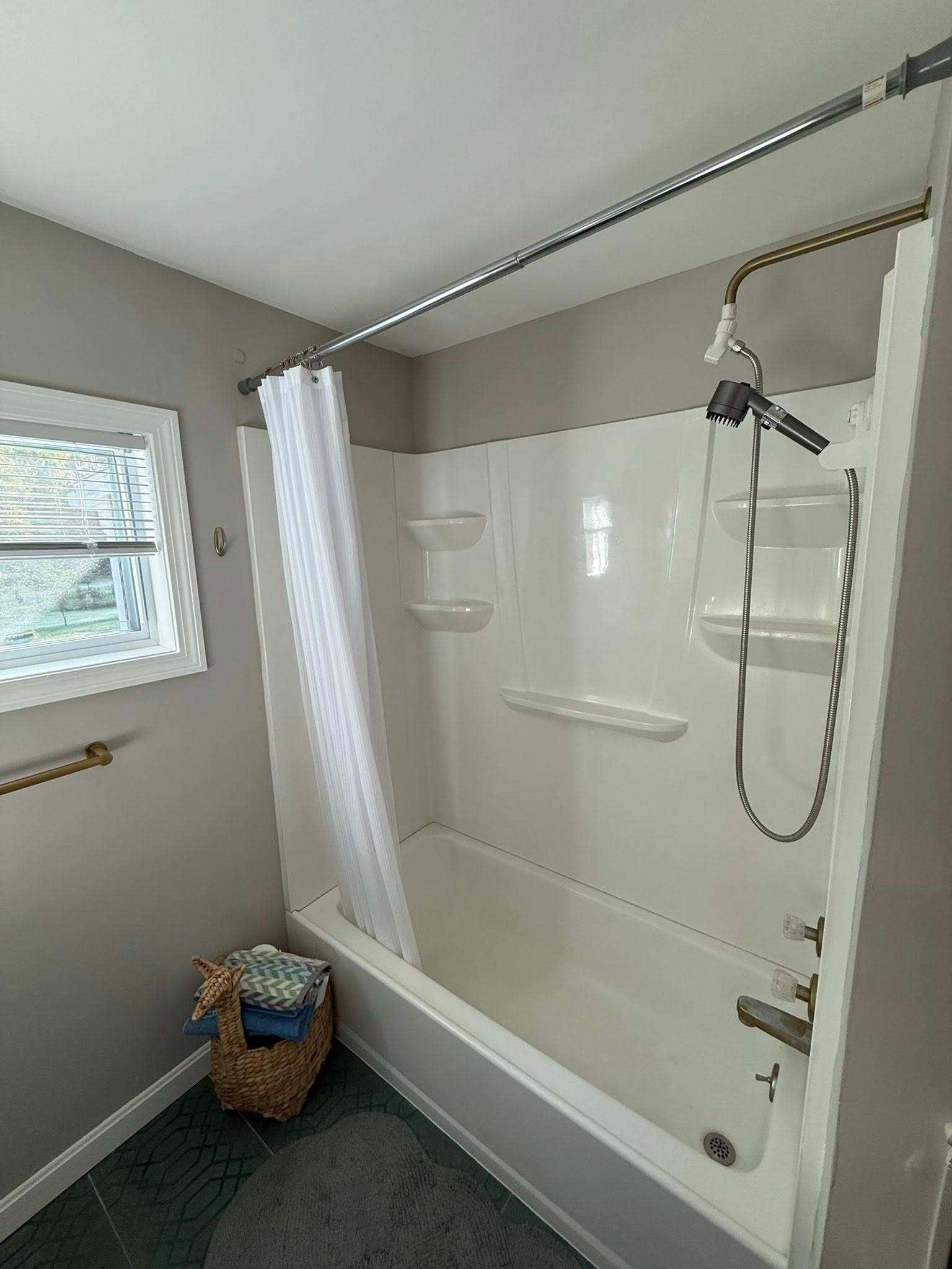 Bathroom with white tub-shower combo, handheld showerhead, window, and shower curtain.