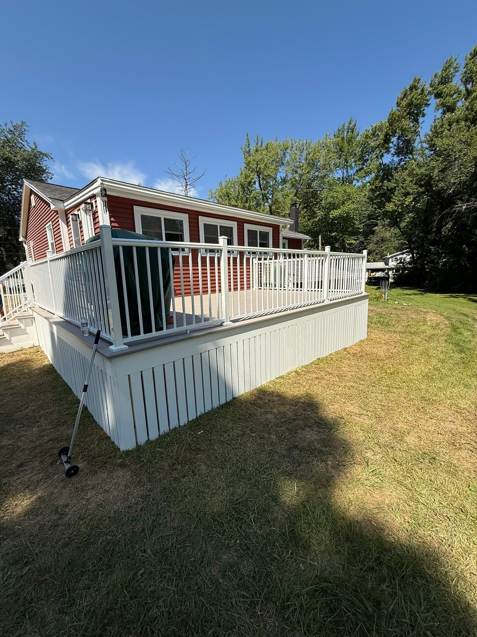 Small white house porch with red trim and white railing in a sunny grassy yard