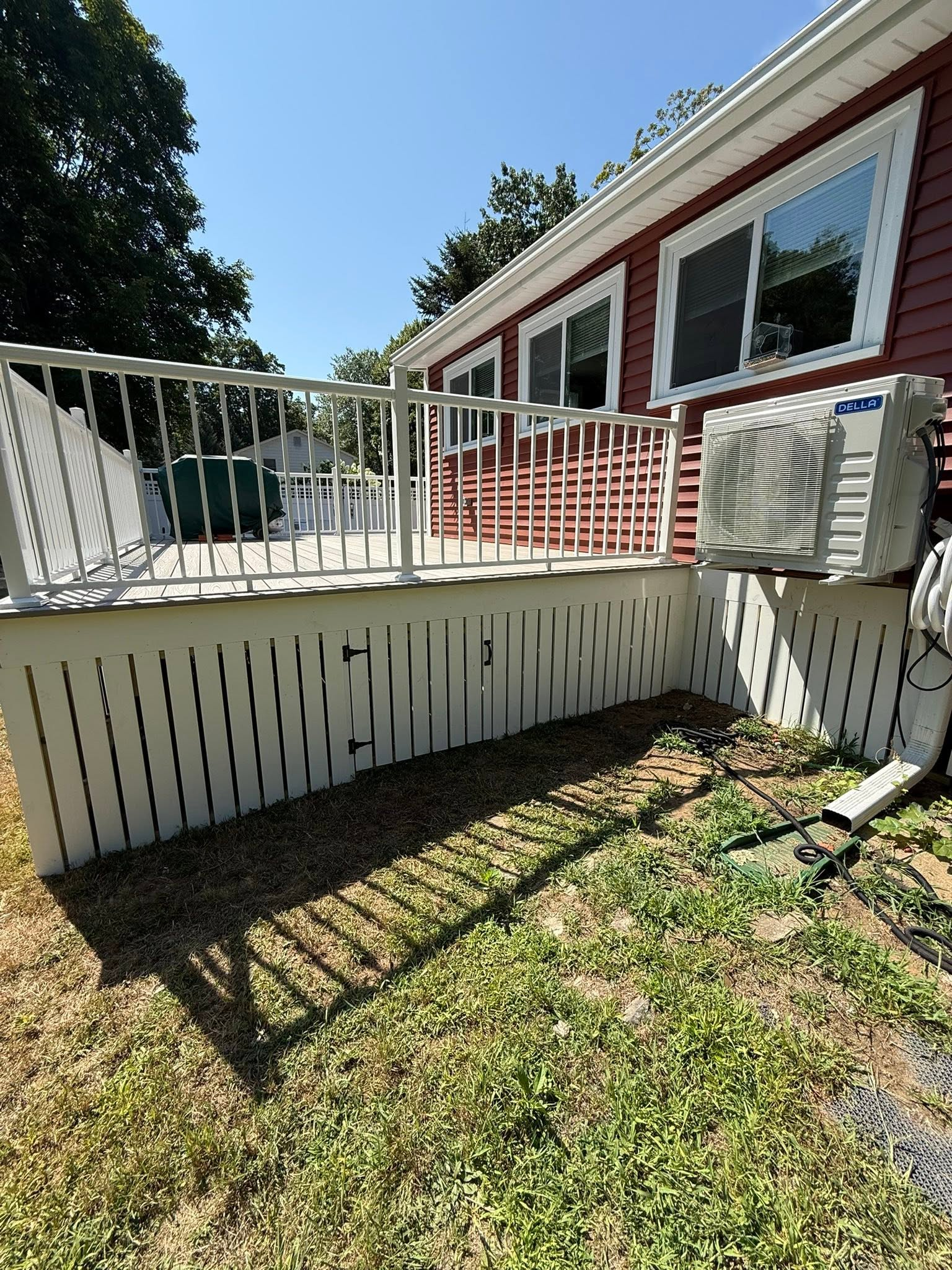 Red house deck with white railing, stairs, and an air-conditioning unit above a brick-and-concrete patio.
