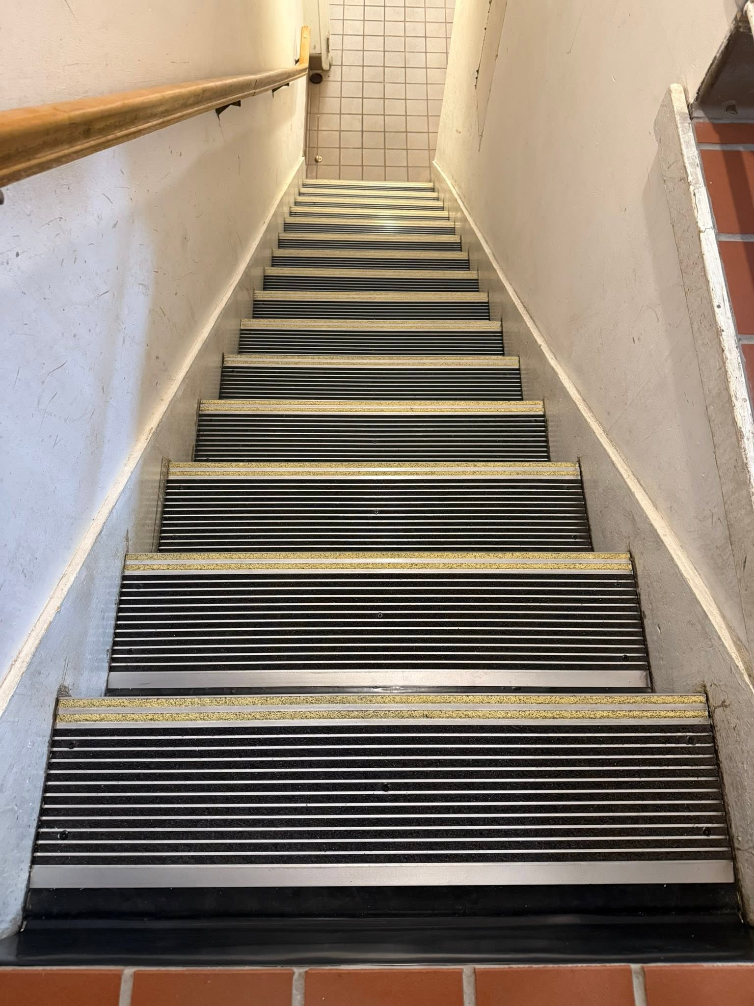 Steep indoor staircase with black nonslip treads and white walls, viewed from the bottom.