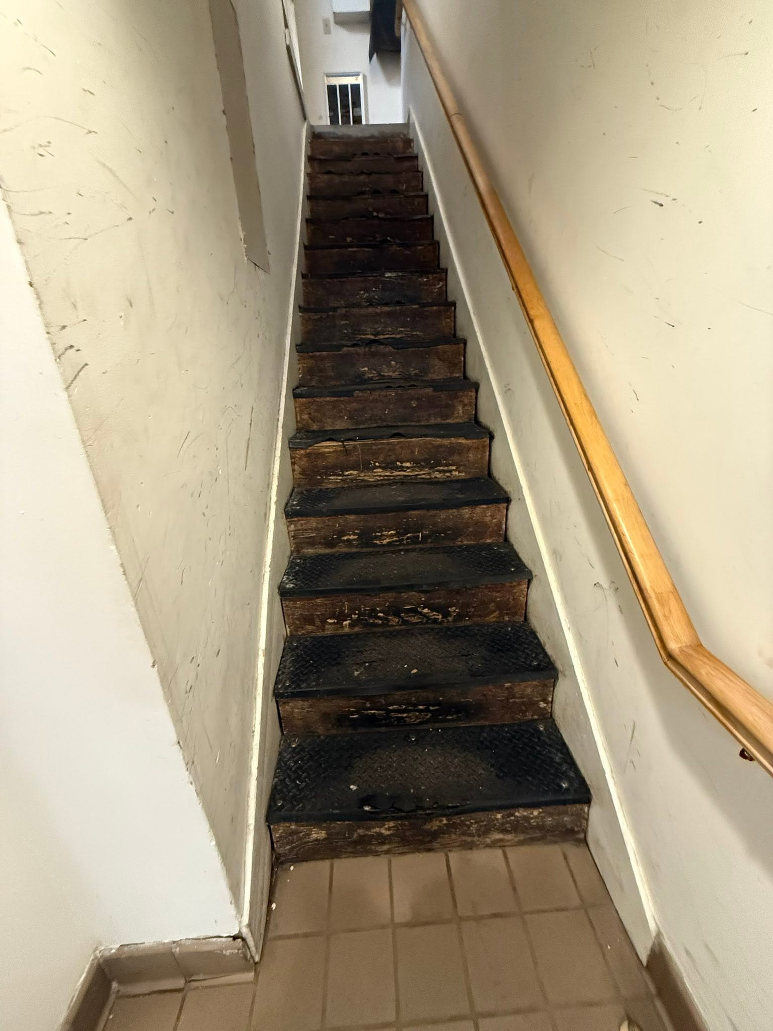 Narrow indoor staircase with worn dark carpet and a wooden handrail along the right wall.