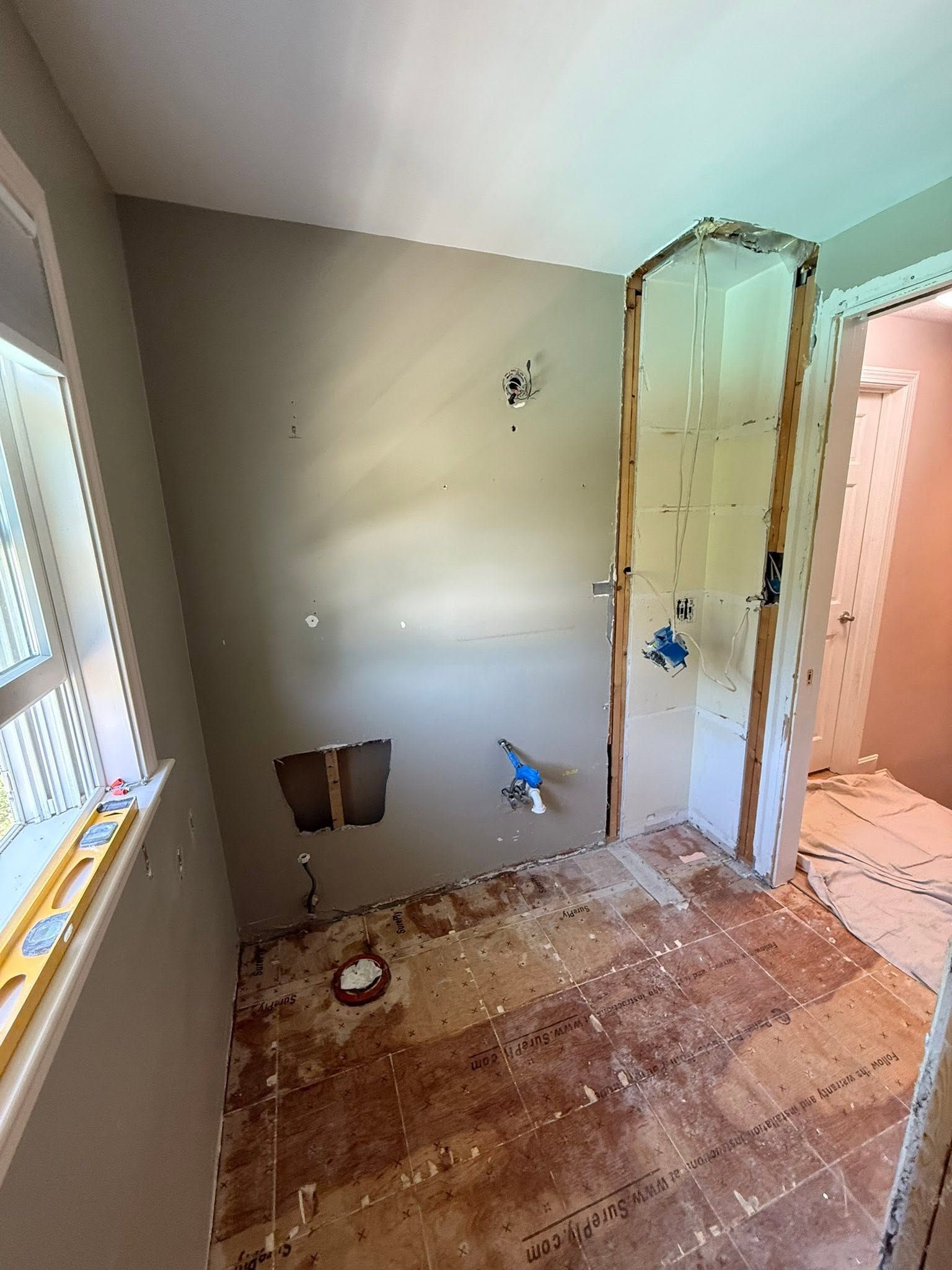 Renovation site with exposed plumbing, unfinished drywall, and bare subfloor in a bathroom.