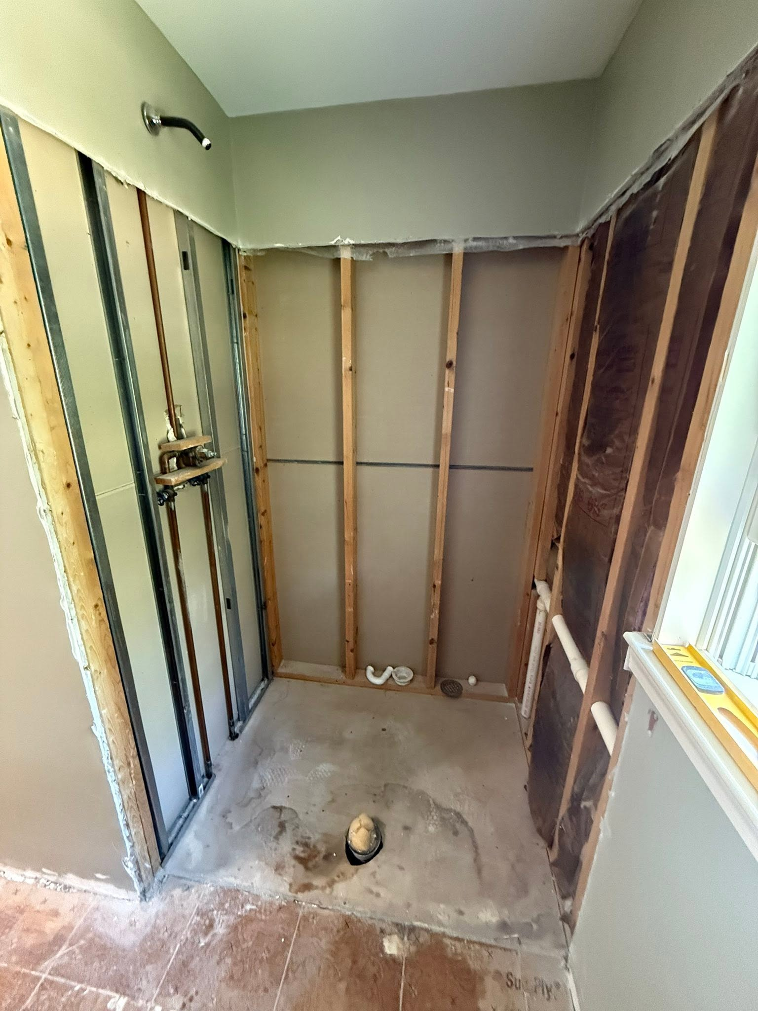 Partially gutted bathroom with exposed studs, drywall removed, and bare concrete floor.