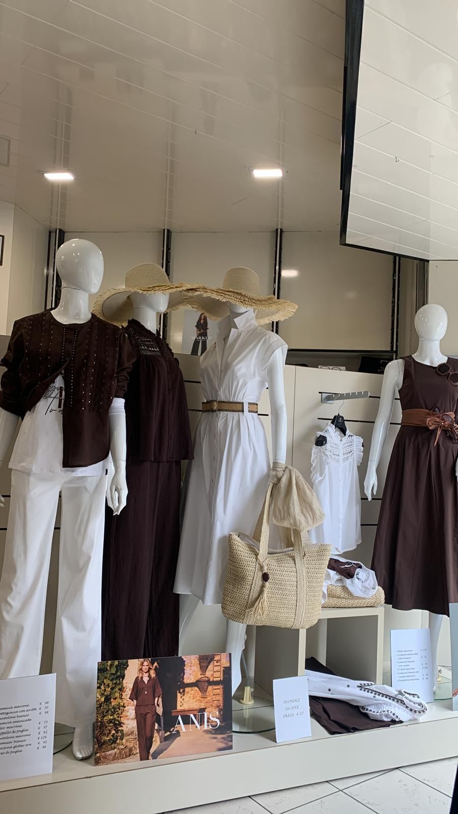 Interno di un negozio di abbigliamento con scaffali pieni di abiti rosa e bordeaux e scaffali espositivi con borse.