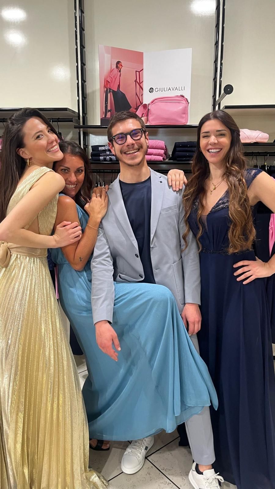 Quattro persone posano in un negozio di abbigliamento: due donne in abito lungo, un uomo in blazer e una donna in abito blu.