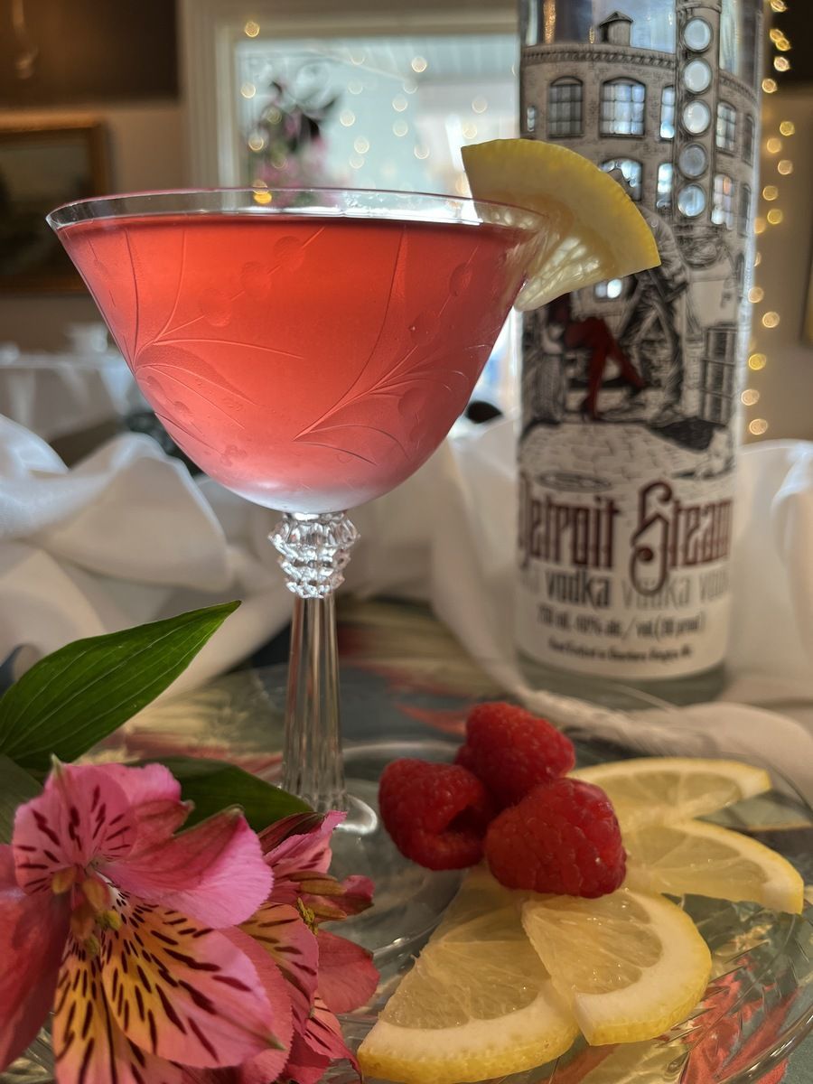 A martini with raspberries and lemon slices next to a bottle of vodka.