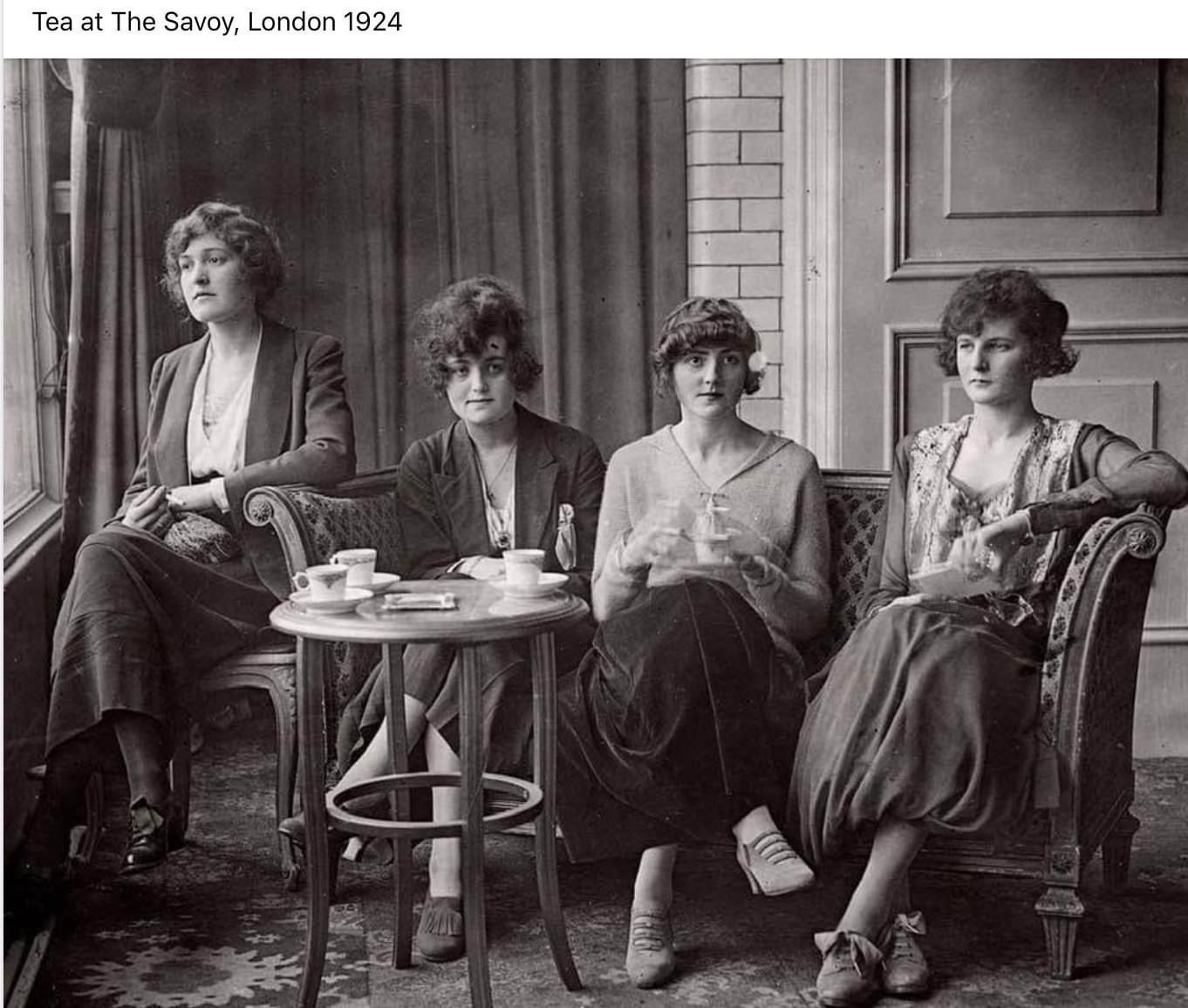 A black and white photo of four women sitting at a table drinking tea