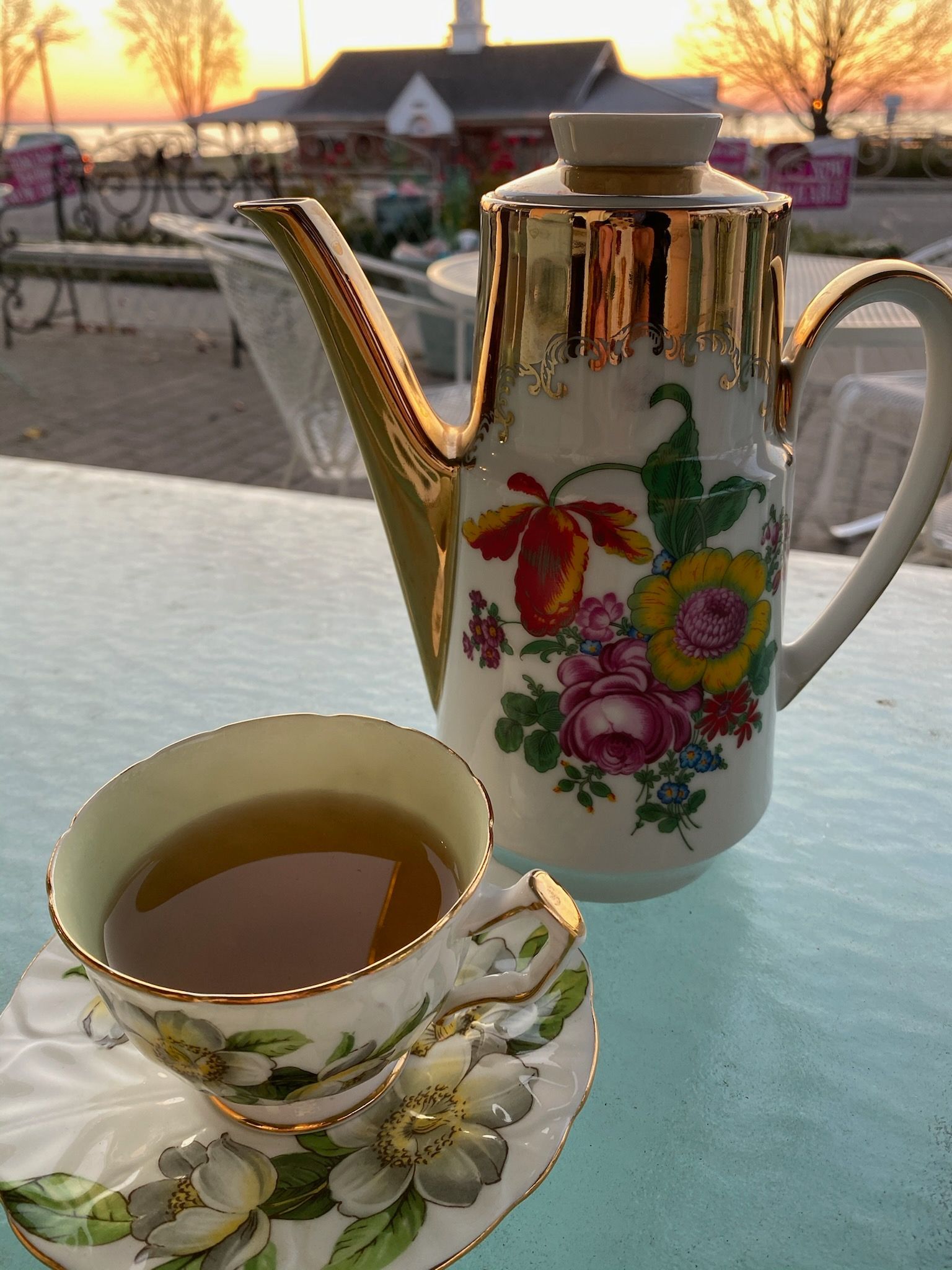 A teapot with flowers on it sits next to a cup of tea.