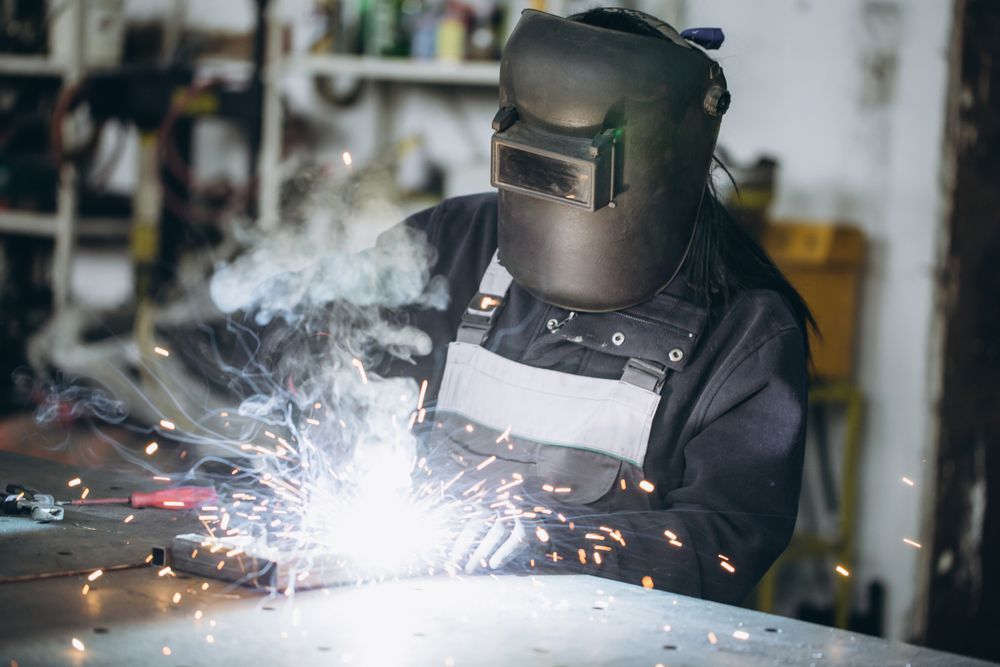 A Woman is Welding a Piece of Metal in a Garage — Febos Welding and Engineering In Shellharbour, NSW