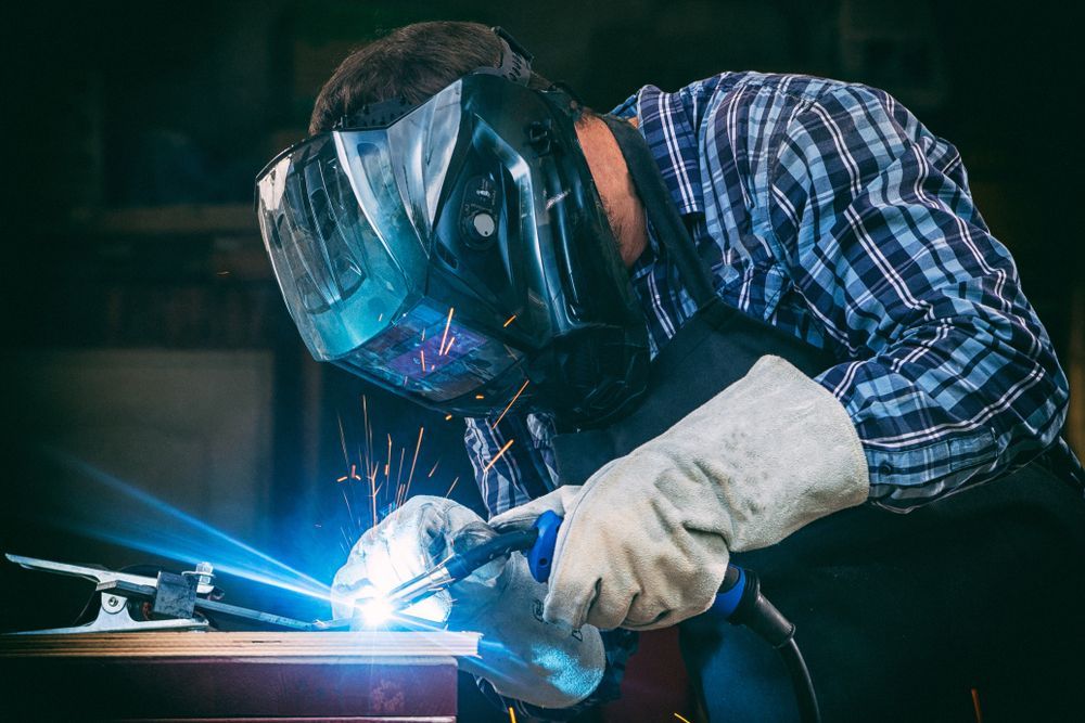 A Man Wearing a Welding Mask and Gloves is Welding a Piece of Metal — Febos Welding and Engineering In Corrimal, NSW