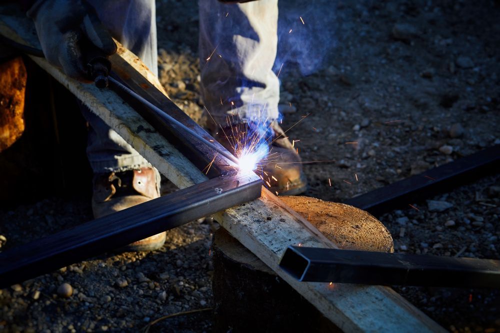 A Man is Welding a Piece of Metal on a Piece of Wood — Febos Welding and Engineering In Corrimal, NSW