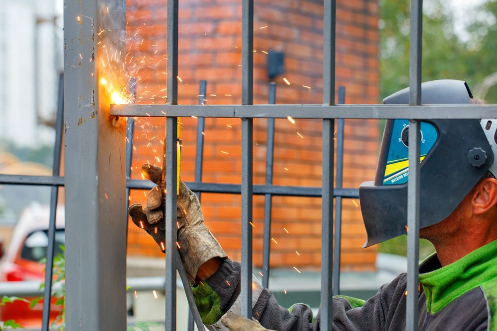 A Man Wearing a Welding Mask is Welding a Metal Fence — Febos Welding and Engineering In Kiama, NSW