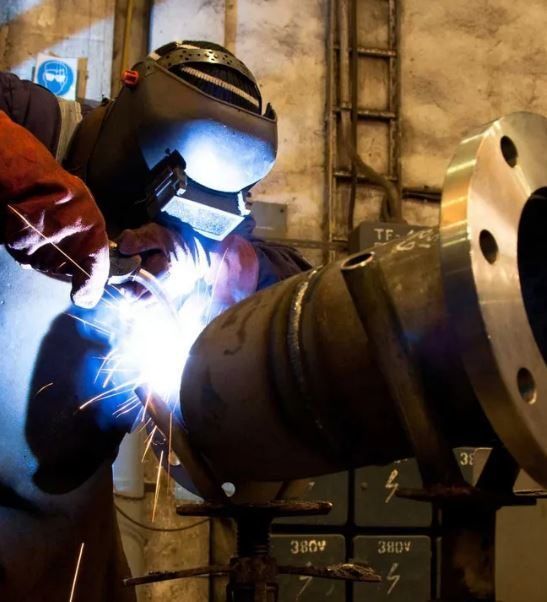 A Man Wearing a Welding Mask is Welding a Pipe — Febos Welding and Engineering In Corrimal, NSW