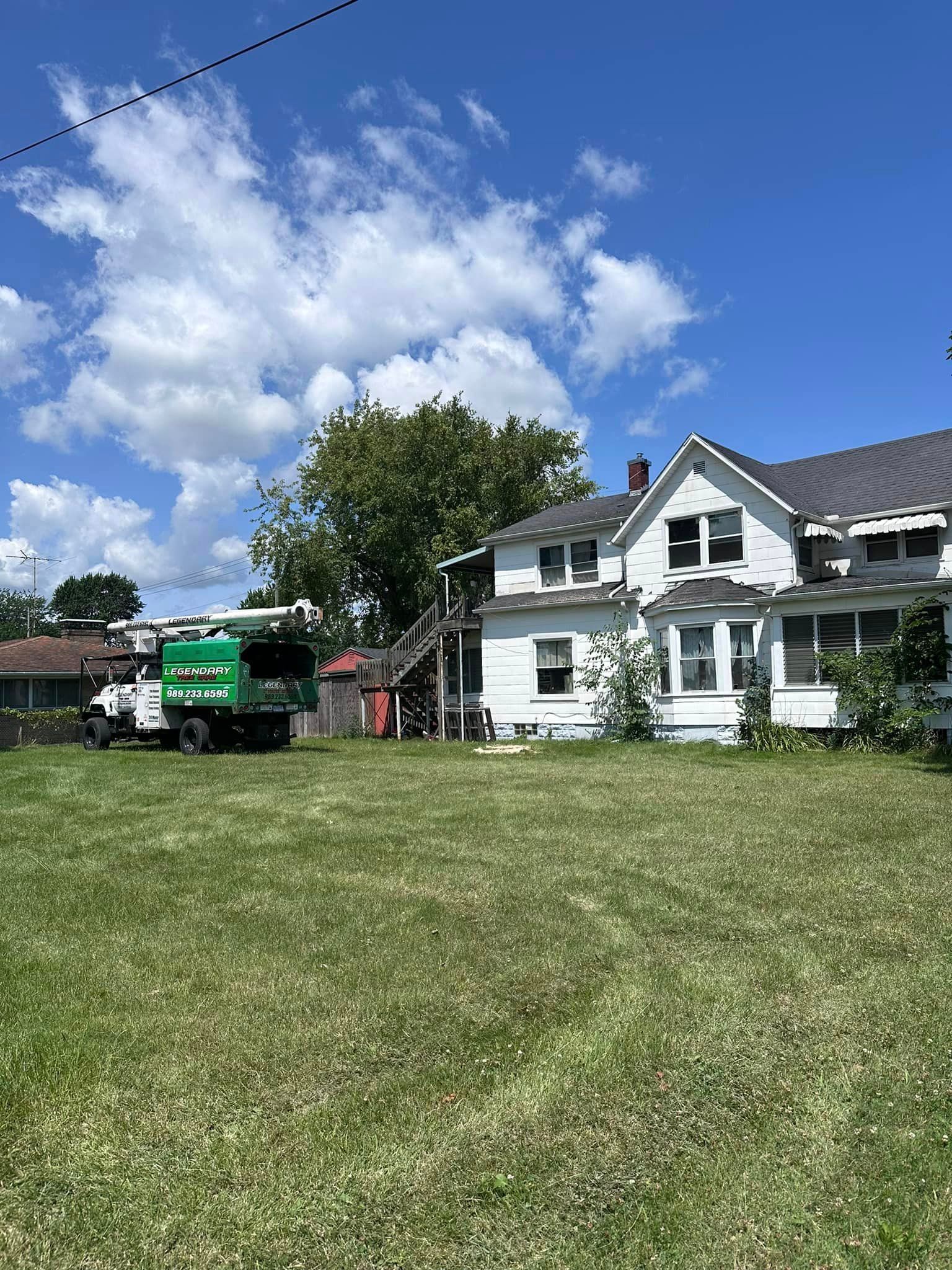 Legendary Tree Care LLC | green garbage truck is parked in front of a white house.