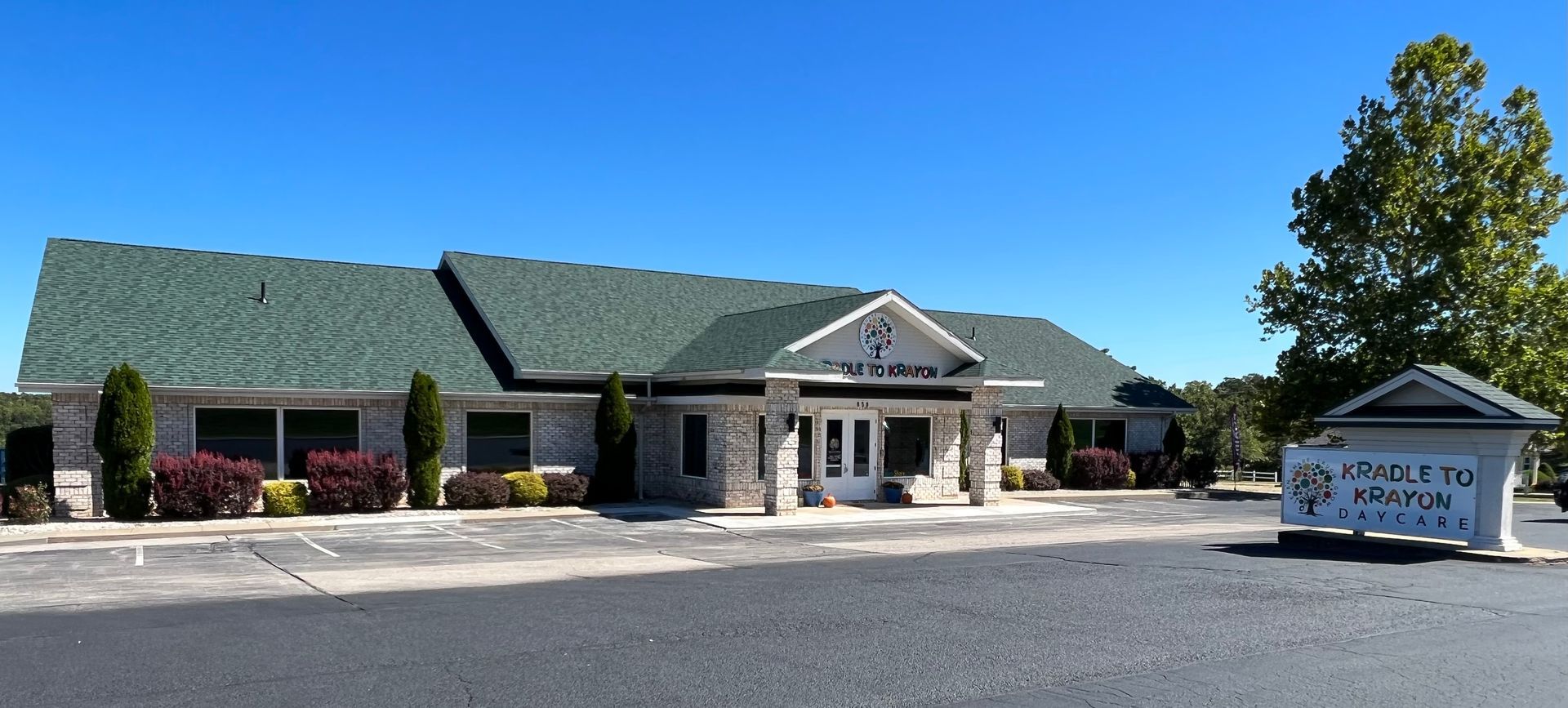 Commercial building with green roof and a sign in front, viewed from a parking lot on a sunny day