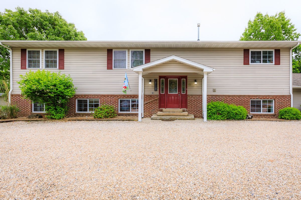 Single-story beige house with red shutters, white columns, and a gravel driveway.