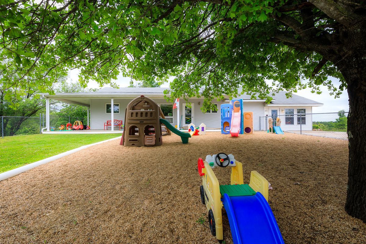 Children’s playground with slides and playhouse under a large tree beside a building.