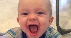 Smiling baby with mouth open, wearing a plaid shirt against a light indoor background
