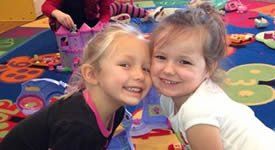 Two children smiling and leaning together on a colorful playroom mat.
