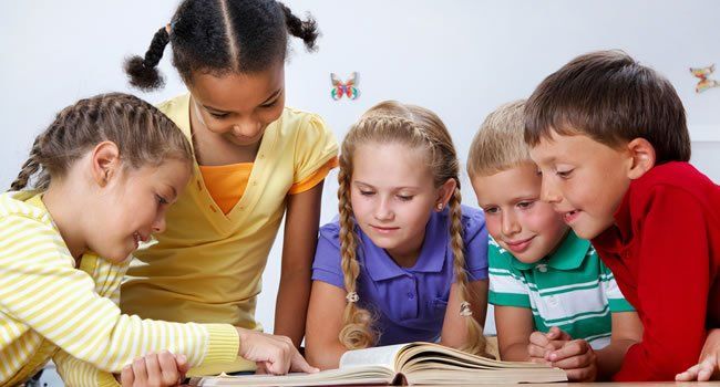 Children gathered around a book, reading together at a table