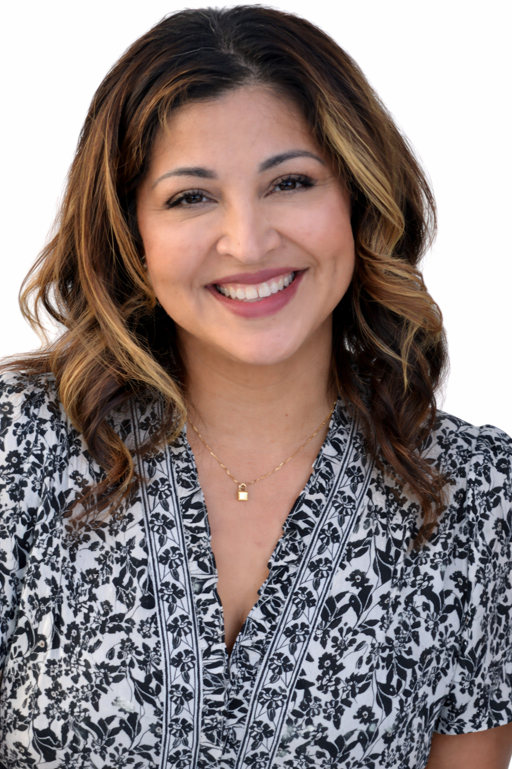 Smiling woman with wavy brown hair in a patterned blouse against a white background