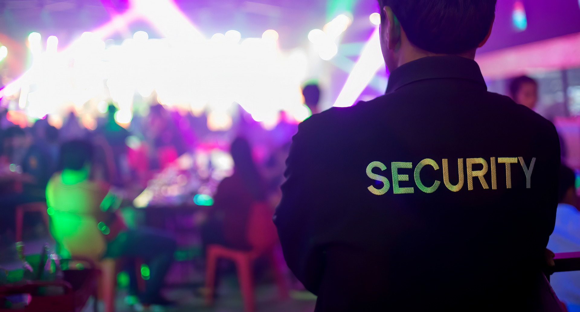 Security guard standing in a neon-lit nightclub with blurred dancers in the background