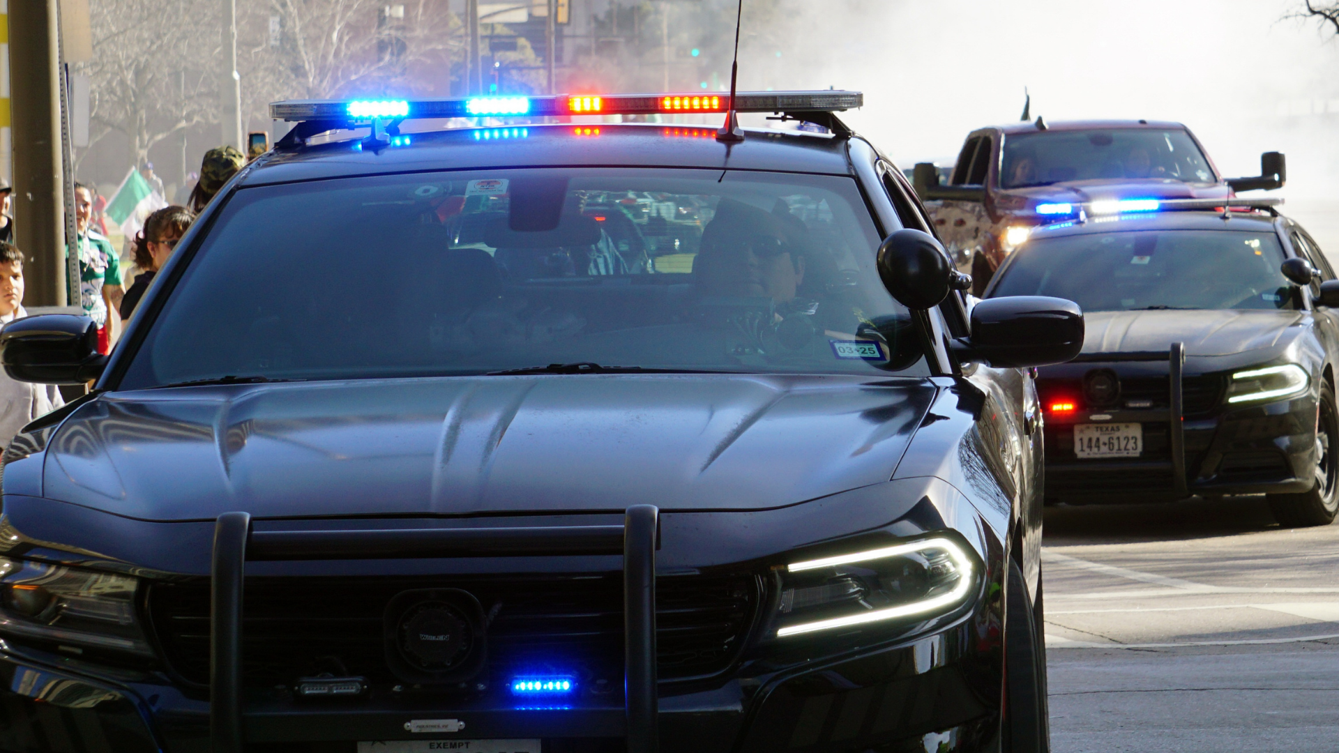 Two black police SUVs with flashing red and blue lights on a street