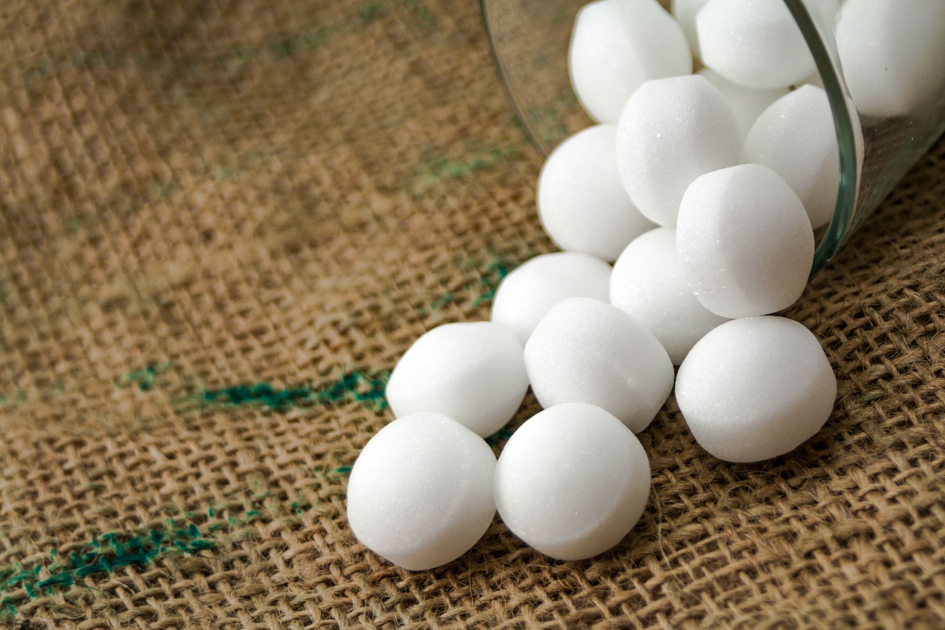 White balls spilling from a clear glass jar onto burlap fabric