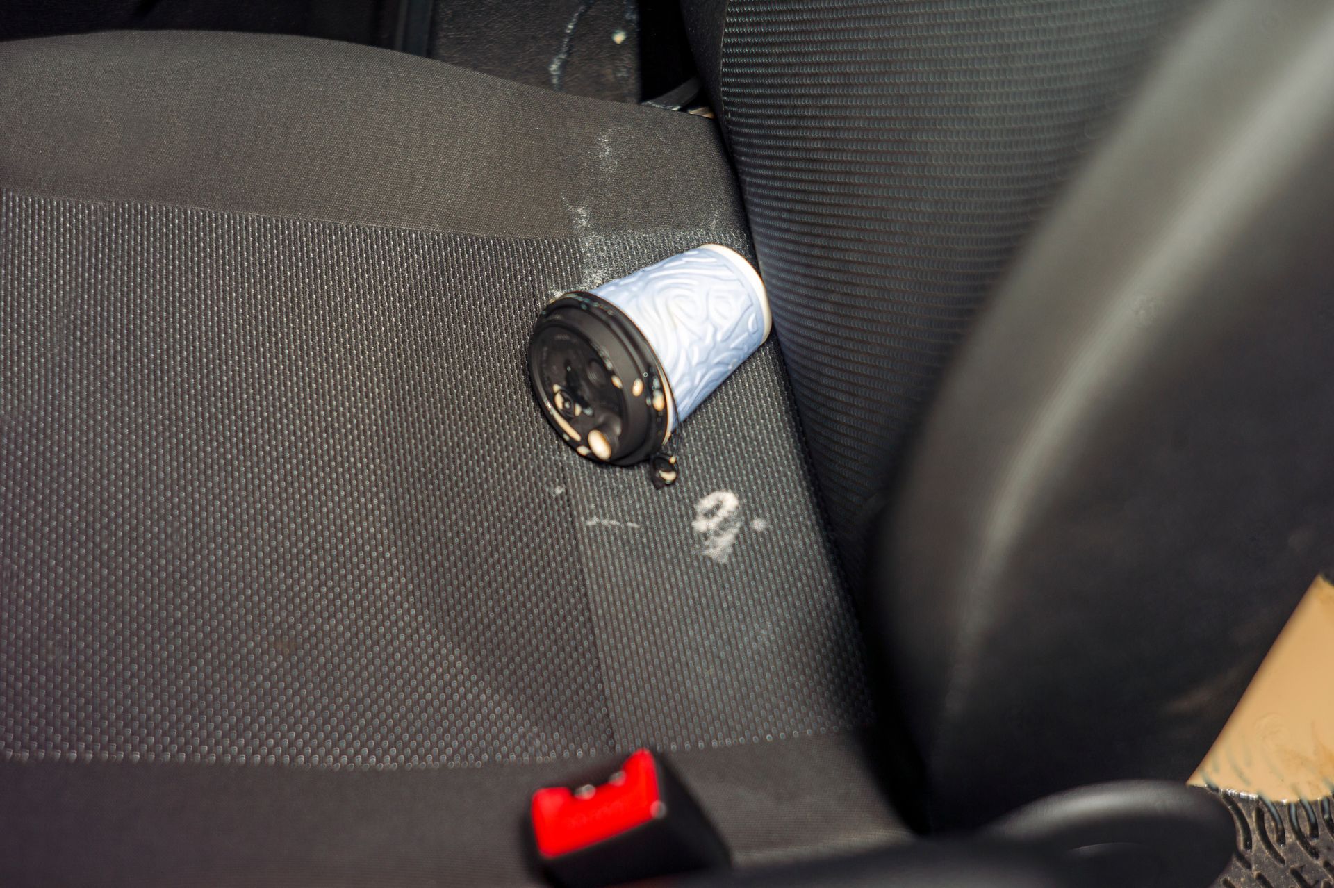 Crushed aluminum can on a car seat next to a red seatbelt buckle Crushed aluminum can on a car seat next to a red seatbelt buckle