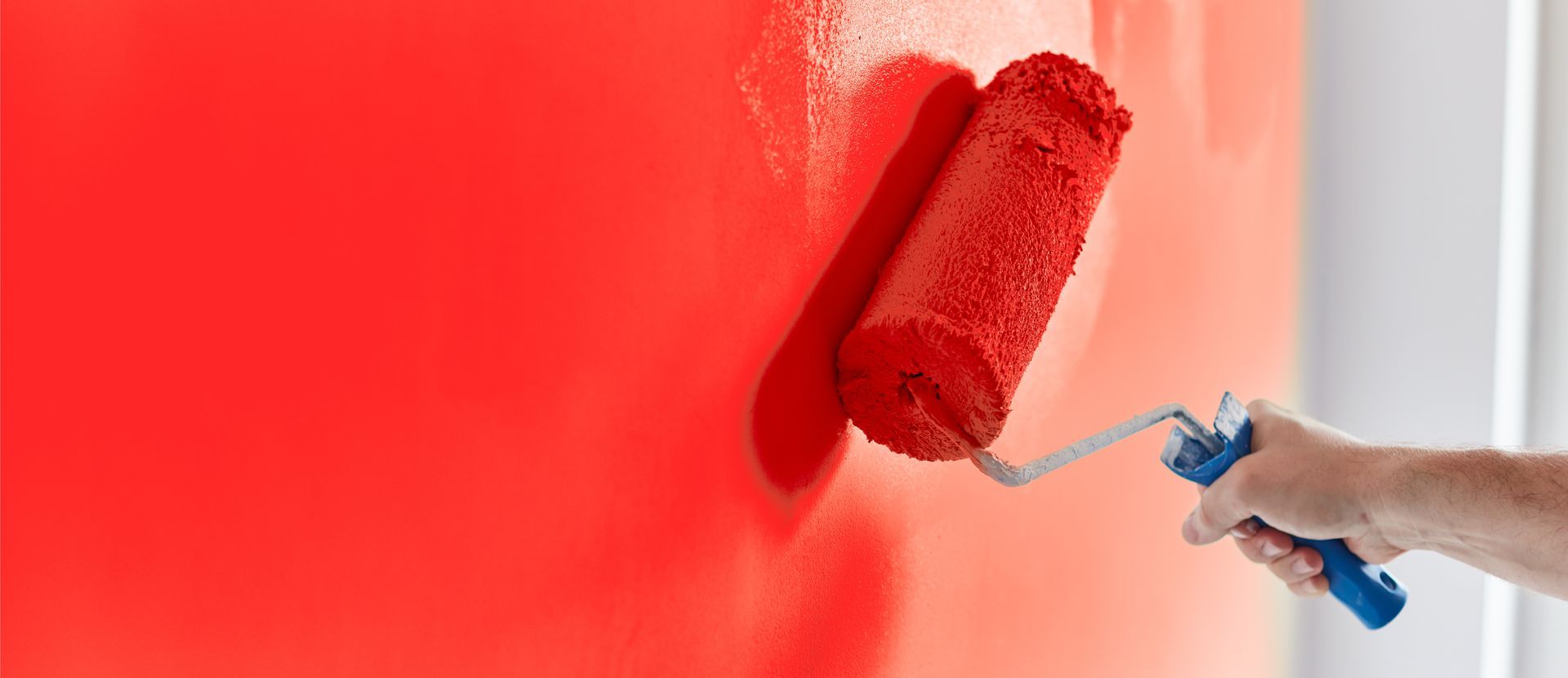 Male hand painting wall with paint roller. Painting apartment, renovating with red color paint 
