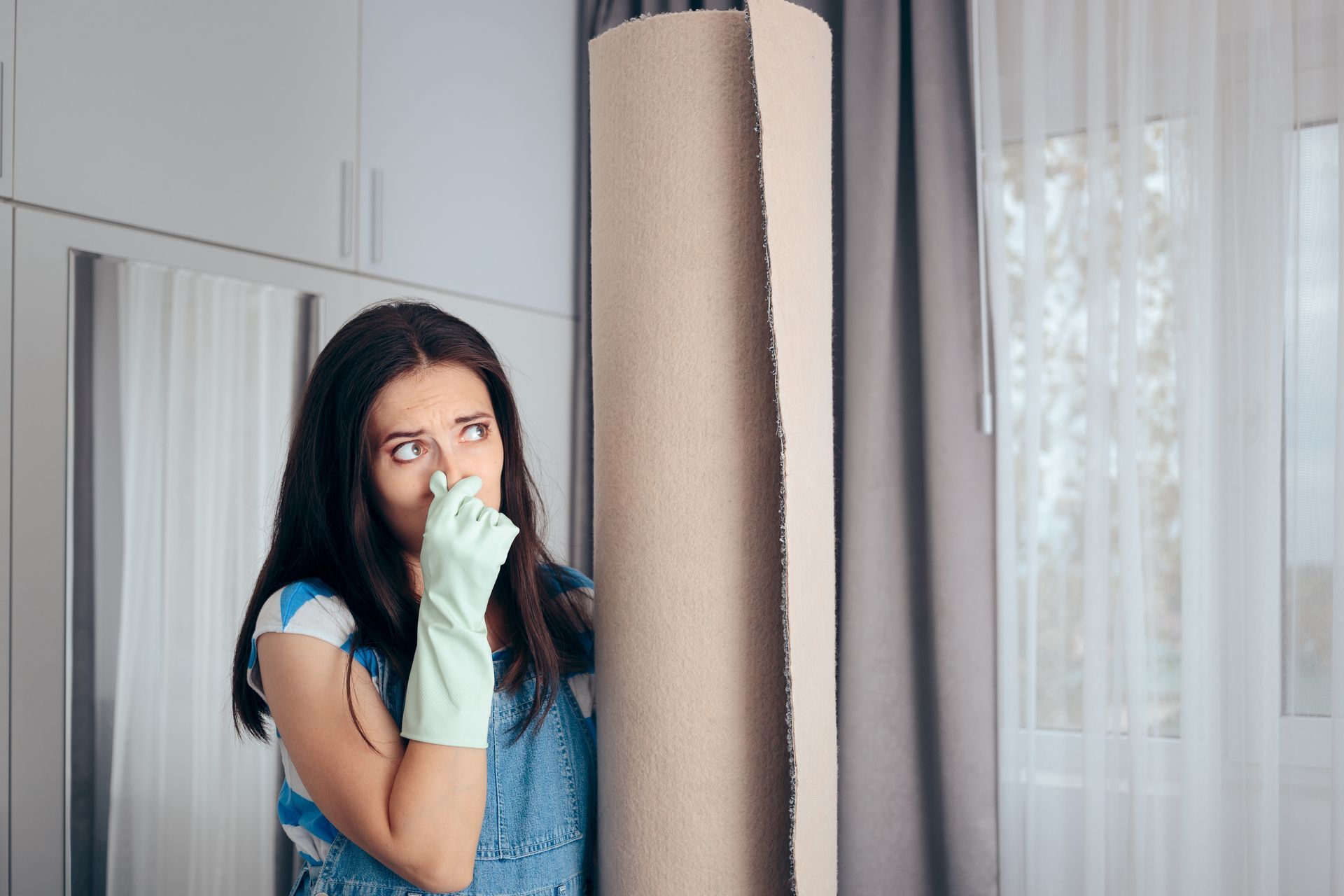 Woman peeking from behind a curtain, covering her nose in a bright room