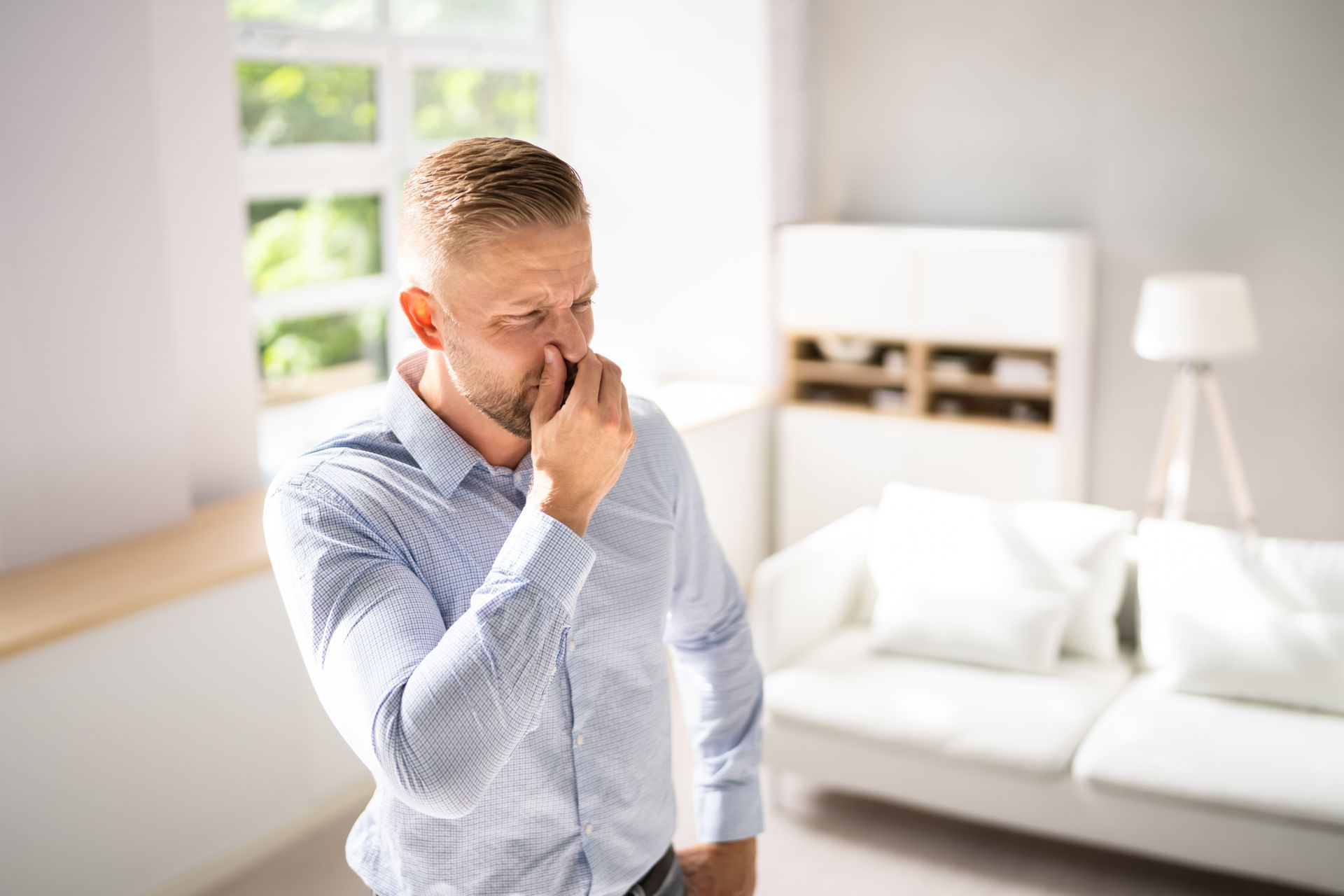 Man standing in a bright living room, pinching his nose with a worried expression