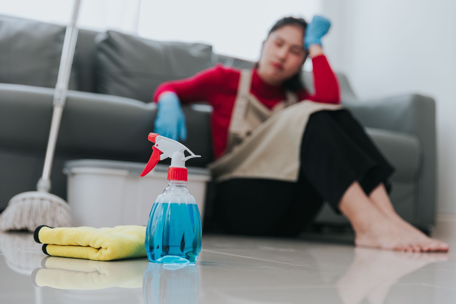 Cleaning spray bottle on floor in foreground, with a person sitting on a couch in the background