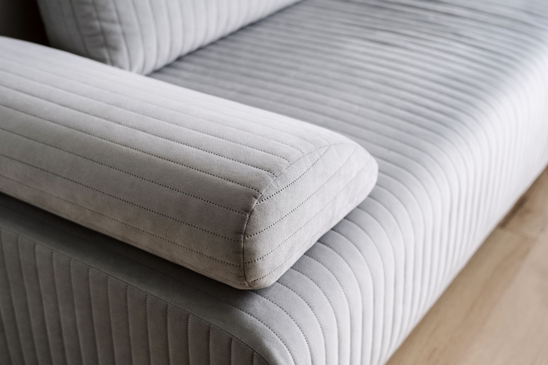A close up of the arm of a grey couch on a wooden floor.