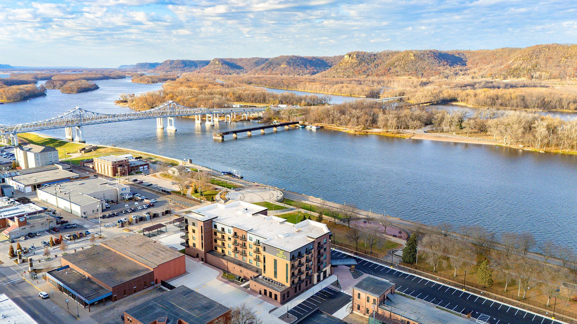 Aerial view of a city next to a river with a bridge, hills, and buildings.