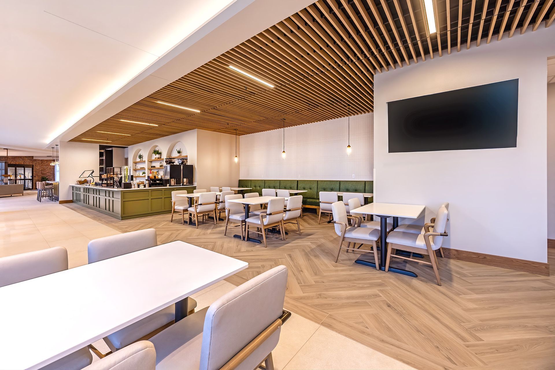 Restaurant interior with tables, chairs, bar, and TV. Wooden ceiling and floor. Green and white decor.