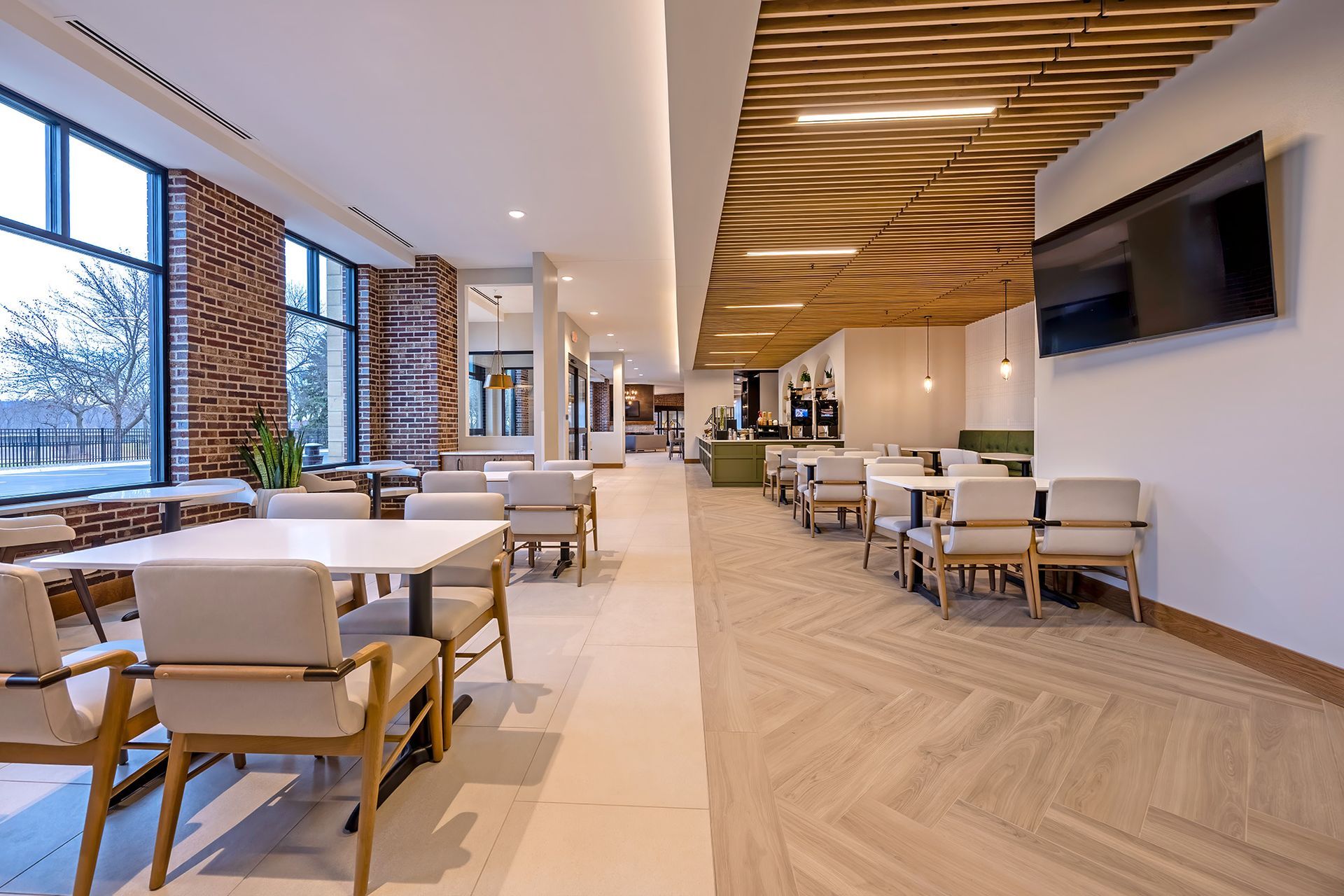 Spacious, well-lit dining area with tables and chairs, large windows, and a wood-paneled ceiling.