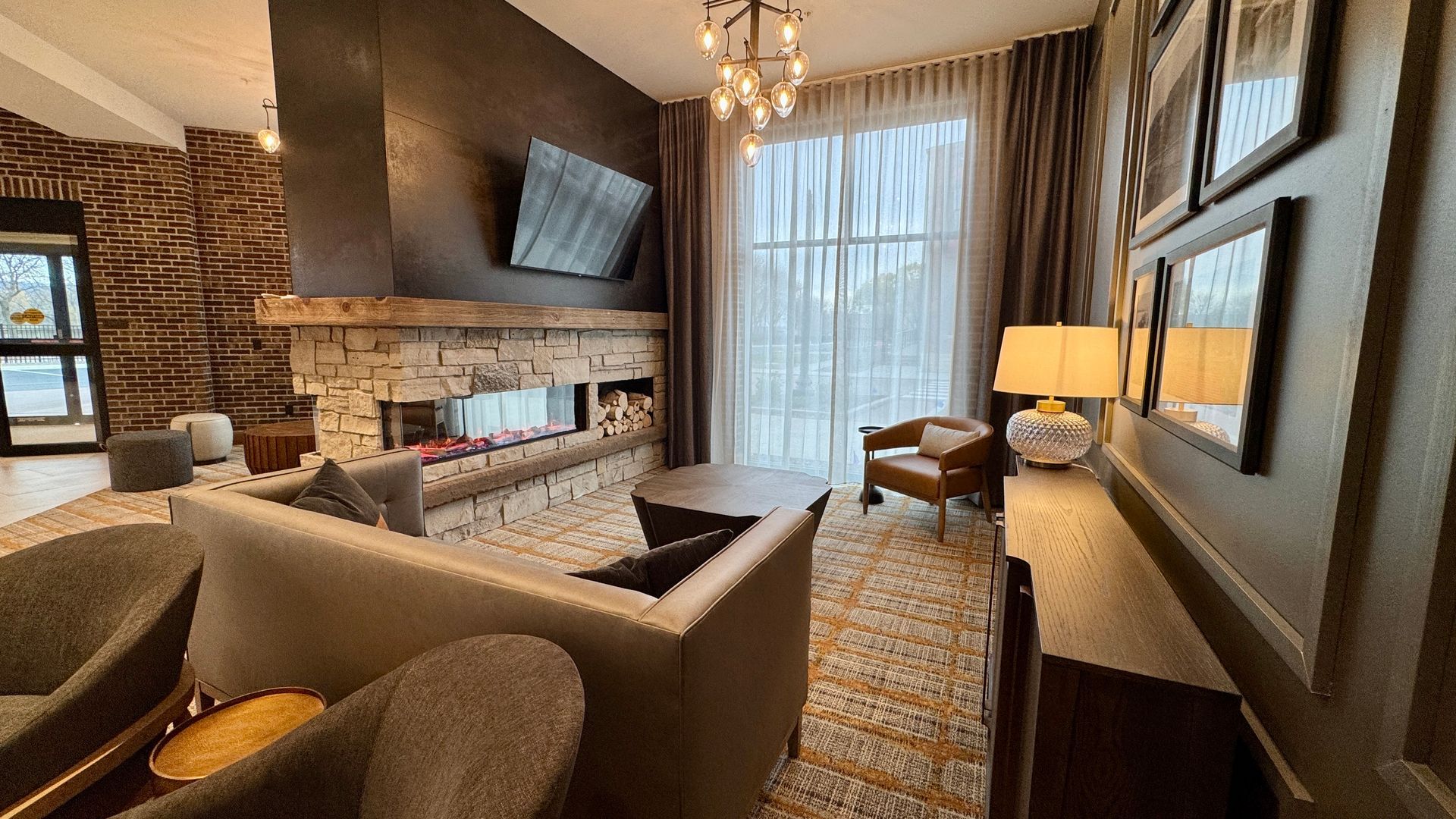 Lounge area with fireplace, sofa, chairs, and window with sheer curtains. Dark wood and stone accents.