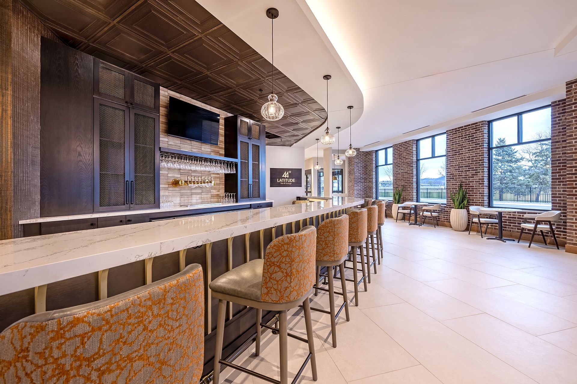 Bar with marble countertop and leather stools. Dark wood cabinetry, large windows, and decorative lighting.