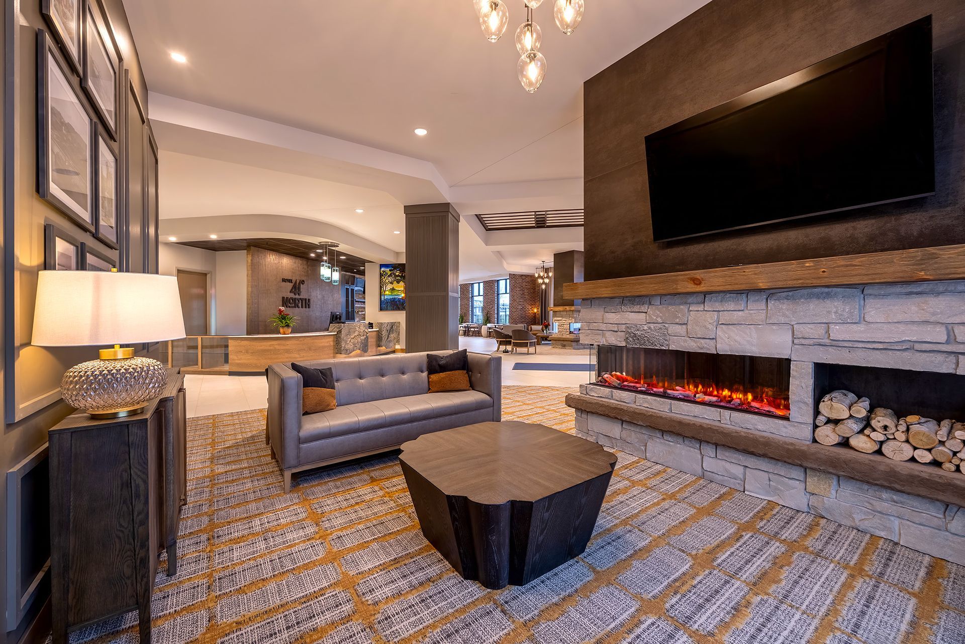 Lounge area with gray sofa, fireplace, TV, wood-like coffee table, and patterned carpet.