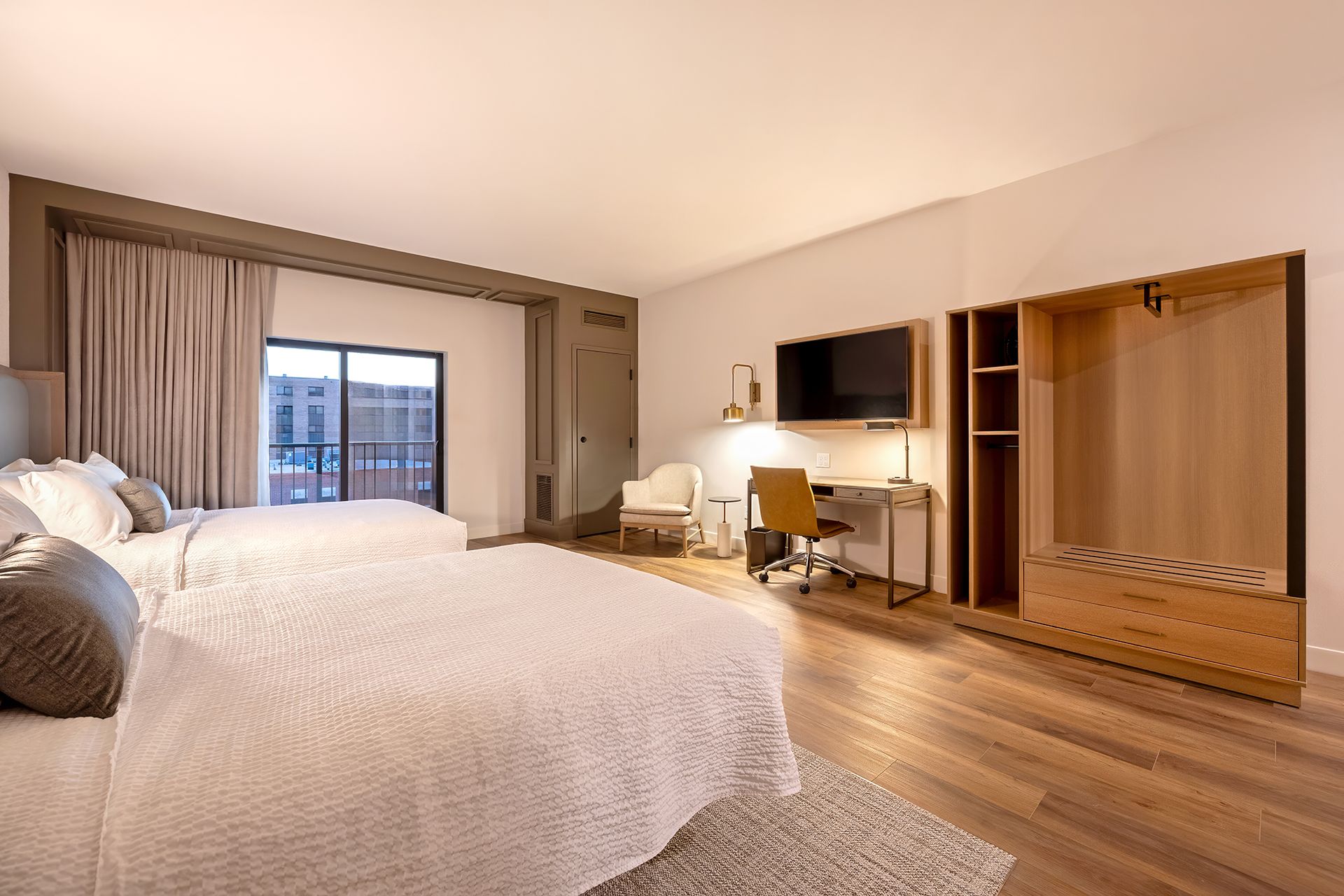 Hotel room with two beds, desk, TV, closet, and balcony with city view.